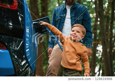 Father with his little son are waiting for electric car to charge Father with his little son are waiting for electric car to charge 128616906