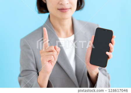一位中年女商界女性拿著智慧型手機，食指向上 128617046