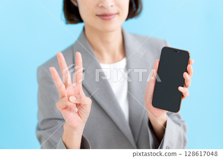 一位中年女商界女性手持智慧型手機,三根手指指向上方 一位中年女商界女性手持智慧型手機,三根手指指向上方 128617048