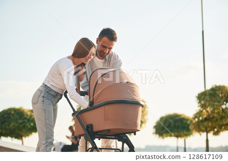 Weekend walk. A young couple with a baby pram are together Weekend walk. A young couple with a baby pram are together 128617109