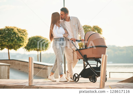 Kissing each other. A young couple with a baby pram is walking together Kissing each other. A young couple with a baby pram is walking together 128617116