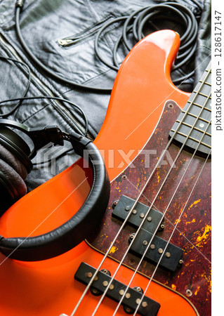 orange electric bass guitar, headphones and cable on a black leather jacket background. 128617147