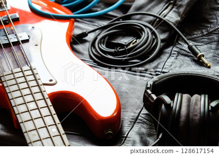 orange electric bass guitar, headphones and cable on a black leather jacket background. 128617154