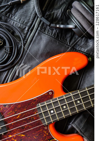 orange electric bass guitar, headphones and cable on a black leather jacket background. 128617161