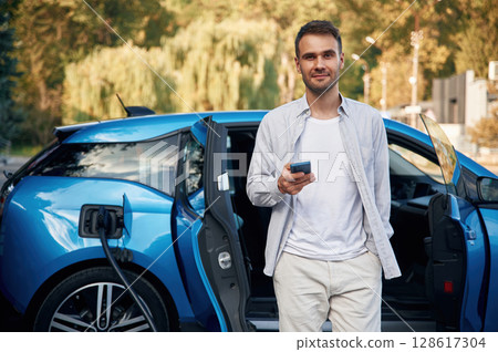 Front view. Man with blue electric car on the charge station Front view. Man with blue electric car on the charge station 128617304