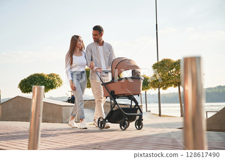 Sunny daytime. A young couple with a baby pram is walking together 128617490