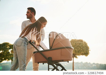 Sunny daytime. A young couple with a baby pram is walking together 128617494