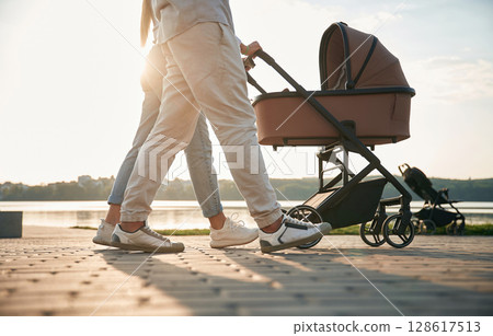 View from below of legs. A young couple with a baby pram is walking together View from below of legs. A young couple with a baby pram is walking together 128617513