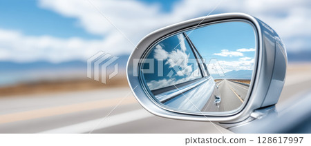 Closeup of car side mirror reflecting clear blue sky with clouds and open road stretching into distance, evoking sense of freedom and travel Closeup of car side mirror reflecting clear blue sky with clouds and open road stretching into distance, evoking sense of freedom and travel 128617997