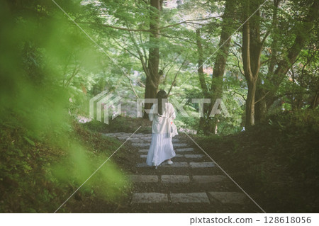 一位女士沿著綠色山坡的通道走向神社 128618056