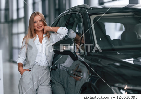 Leaning on the automobile. Woman in formal clothes is in the car dealership 128618095