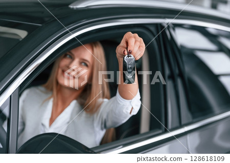Keys from new car. Woman in formal clothes is indoors in the auto salon Keys from new car. Woman in formal clothes is indoors in the auto salon 128618109