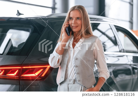 Conversation by the phone. Woman in formal clothes is in the car dealership 128618116