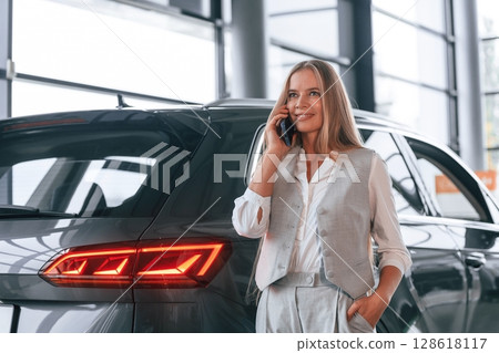 Conversation by the phone. Woman in formal clothes is in the car dealership Conversation by the phone. Woman in formal clothes is in the car dealership 128618117