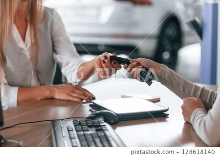 Sitting by the table. Female manager is helping woman customer in the car dealership salon 128618140