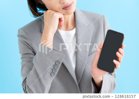 A middle-aged business woman looking at her smartphone and worrying 128618157
