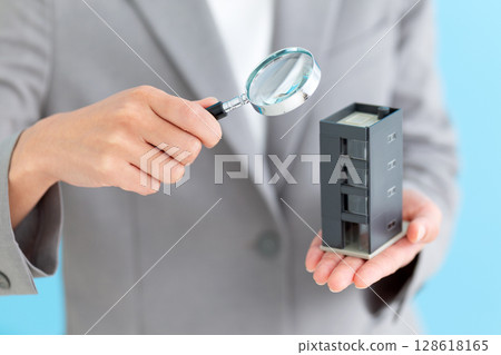Middle-aged female business woman holding a model of an office building and a magnifying glass 128618165