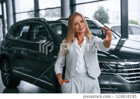 Holding keys. Woman in formal clothes is in the car dealership Holding keys. Woman in formal clothes is in the car dealership 128618195