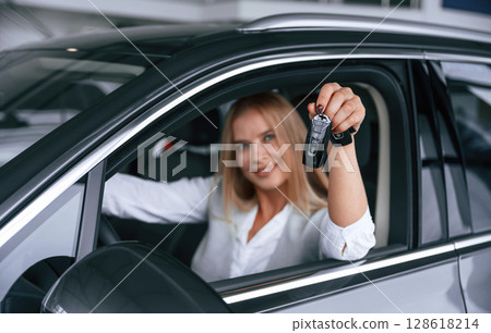 Keys from new car. Woman in formal clothes is indoors in the auto salon Keys from new car. Woman in formal clothes is indoors in the auto salon 128618214