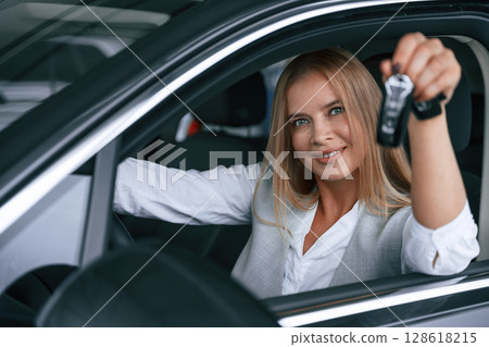 Keys from new car. Woman in formal clothes is indoors in the auto salon Keys from new car. Woman in formal clothes is indoors in the auto salon 128618215