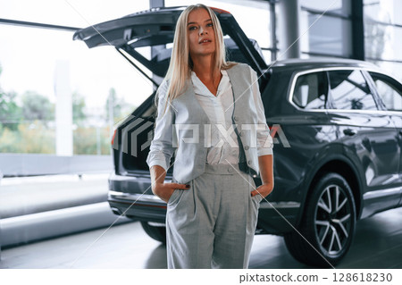 Hood is opened. Woman in formal clothes is in the car dealership 128618230