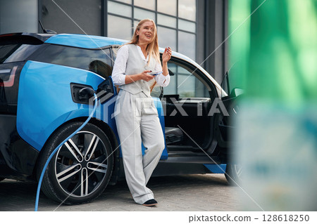Woman on the electric cars charge station at daytime 128618250