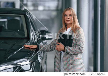 With tablet in hands. Woman in formal clothes is in the car dealership 128618262