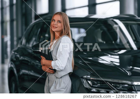 Leaning on the automobile. Woman in formal clothes is in the car dealership 128618267