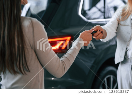 Giving the keys. Female manager is helping woman customer in the car dealership salon Giving the keys. Female manager is helping woman customer in the car dealership salon 128618287