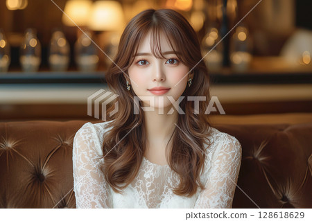 Elegant young woman wearing lace top sitting on sofa in club room 128618629