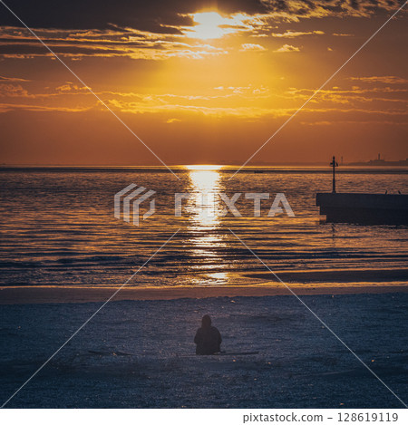 A silhouetted figure against the orange glow of the setting sun 128619119