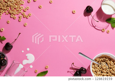 Grain rings, cherries, mint leaves, a spoon, spilled milk, and a bowl on pink background. A breakfast concept with space for your text. Grain rings, cherries, mint leaves, a spoon, spilled milk, and a bowl on pink background. A breakfast concept with space for your text. 128619159