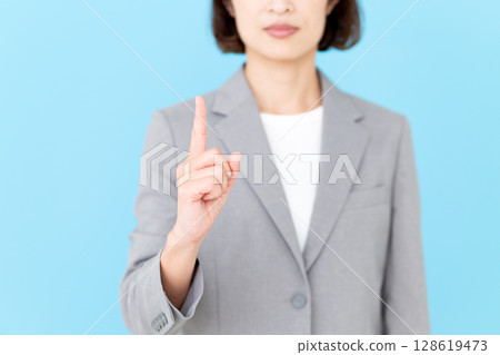A middle-aged female business woman wearing a gray suit and pointing her index finger up A middle-aged female business woman wearing a gray suit and pointing her index finger up 128619473