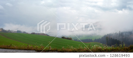 Autumn panoramic view of green valley and foggy wooded hills 128619493