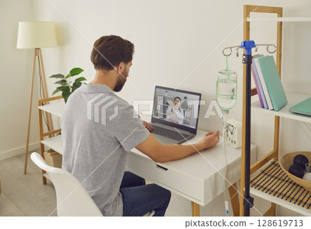 Man having online video call with doctor at home while receiving IV drip infusion Man having online video call with doctor at home while receiving IV drip infusion 128619713
