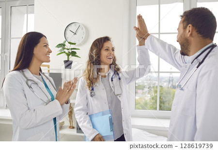 Doctors rejoicing at success in treatment giving high five each other standing in clinic 128619739