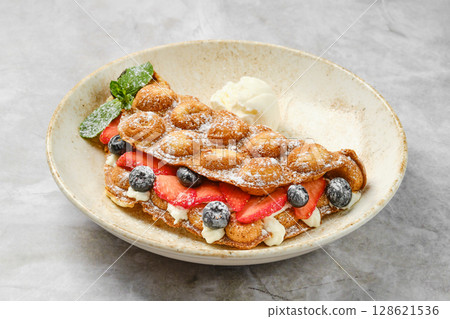 Delicious dessert featuring bubble waffles with strawberries, blueberries, and ice cream Delicious dessert featuring bubble waffles with strawberries, blueberries, and ice cream 128621536