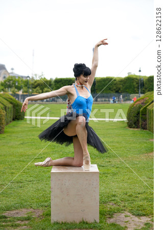 Ballet dancer posing on stone pedestal in garden 128622158