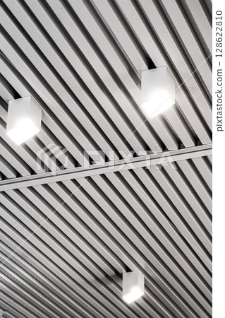 Ceiling with bright lights in a modern warehouse, shopping center building, office or commercial real estate object. Directional LED lights on rails under the ceiling Ceiling with bright lights in a modern warehouse, shopping center building, office or commercial real estate object. Directional LED lights on rails under the ceiling 128622810