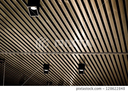 Bottom view of lath ceiling with spot lights. Abstract modern architecture or interior background in black and white with geometric structure. 128622848