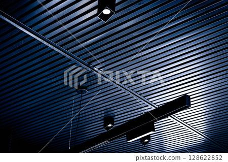 Bottom view of lath ceiling with spot lights. Abstract modern architecture or interior background in black and white with geometric structure. 128622852