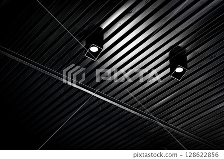 Bottom view of lath ceiling with spot lights. Abstract modern architecture or interior background in black and white with geometric structure. 128622856