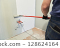 A man paints walls with a roller, working painting on the surface, painting walls in an apartment, repairing with white paint. With space to copy. High quality photo 128624164