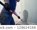 A worker paints the inner wall of his house. Apartment renovation. Concrete walls are painted gray with a paint roller. High quality photo 128624166