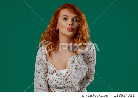 Playful ginger woman sends air kiss with gentle hand motion, warm emotional tone 128624321