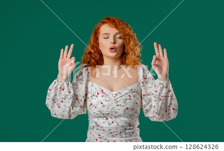 Tranquil woman relaxing, meditating, refuses stress. Red-haired lady breathes deeply, calms down, green studio background. Yoga, moral balance, zen concept. Tranquil woman relaxing, meditating, refuses stress. Red-haired lady breathes deeply, calms down, green studio background. Yoga, moral balance, zen concept. 128624326