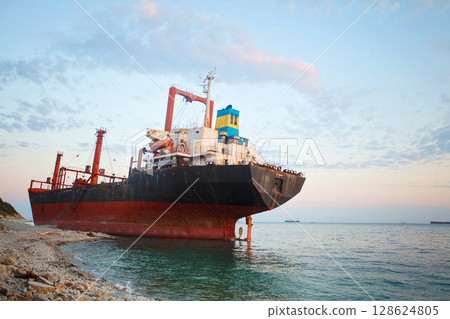 Bulk ship stranded in a sea under sunset sky with white clouds 128624805