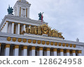 VDNKh USSR Pavilion with Gleaming Golden Soviet Emblem atop Classical White Columns under a Soft Overcast Sky 128624958