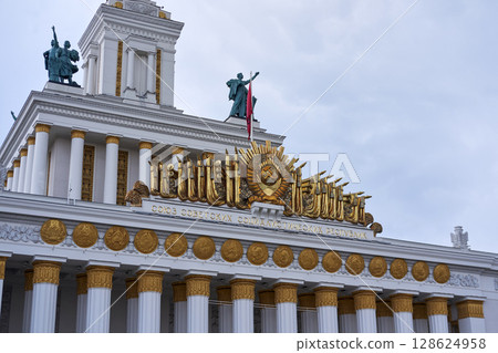 VDNKh USSR Pavilion with Gleaming Golden Soviet Emblem atop Classical White Columns under a Soft Overcast Sky 128624958