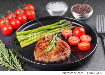 Grilled beef steak with asparagus and cherry tomatoes on black plate, gourmet healthy dinner Grilled beef steak with asparagus and cherry tomatoes on black plate, gourmet healthy dinner 128625872